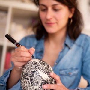 Artist decorating an ostrich egg using a black Posca paint pen